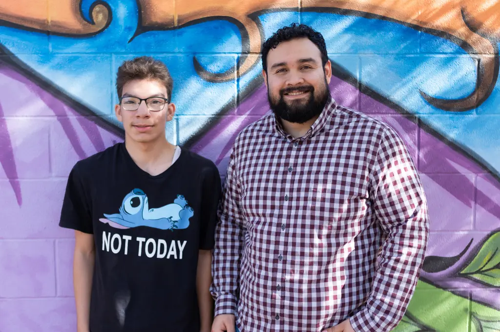Two men posing together in front of a blue and colorful mural background.