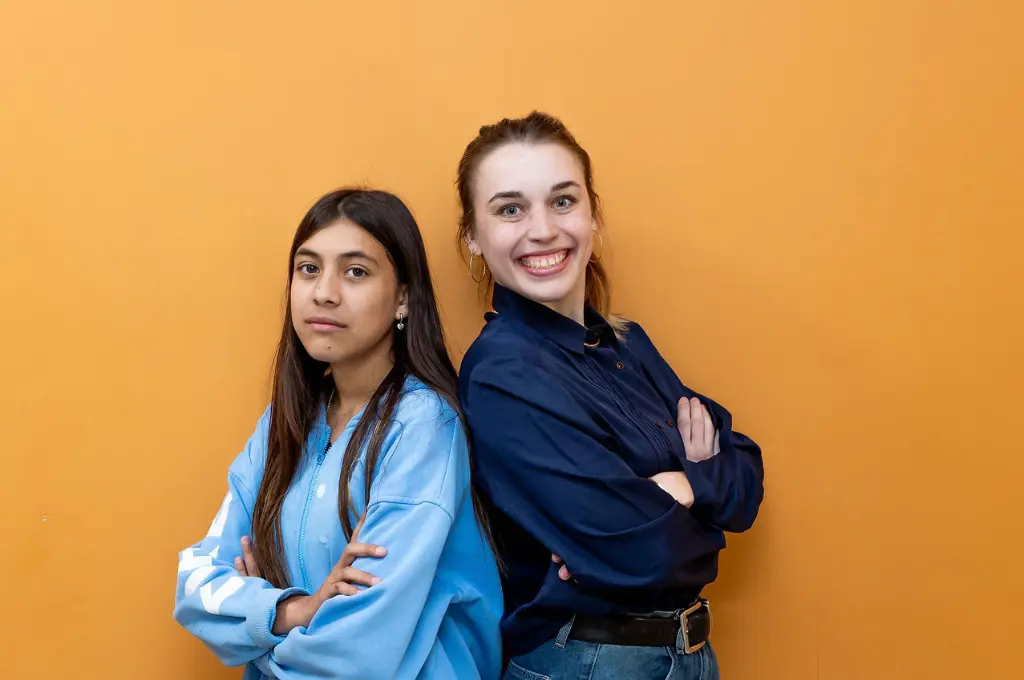 Two young women posing together against a yellow and orange background.