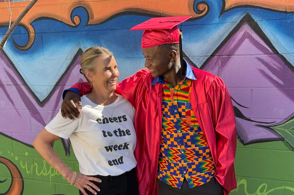Two people posing together in front of a colorful street art or mural background.